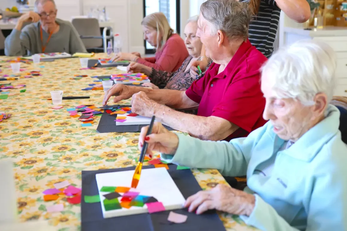 Senior residents participating in arts and crafts activity in assisted living community, caregiver leading creative therapy session