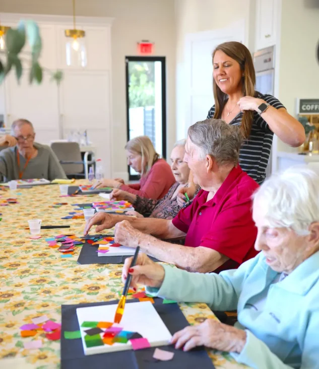 Senior residents participating in arts and crafts activity in assisted living community, caregiver leading creative therapy session
